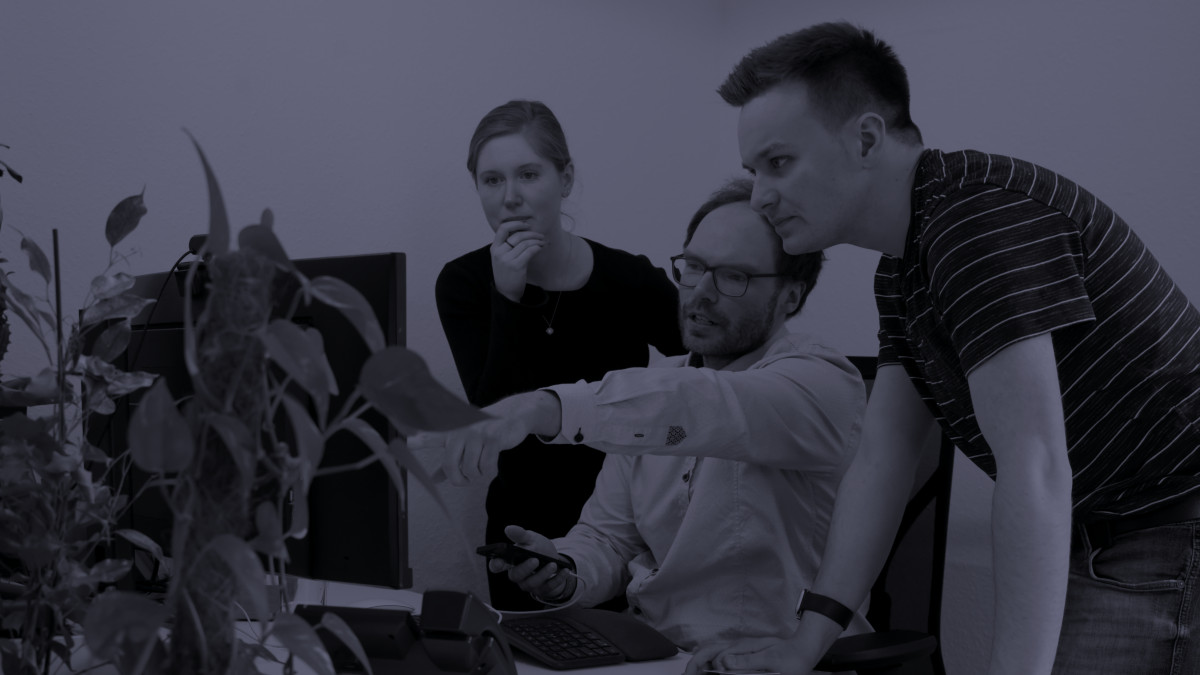 Drei Personen diskutieren etwas vor einem Monitor.