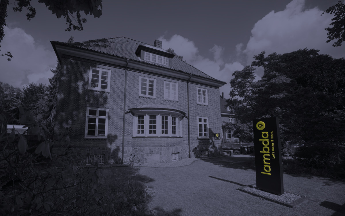 Frontansicht einer Villa im Grünen. Neben der Villa steht ein Leuchtschild mit dem Text „lambda9“.